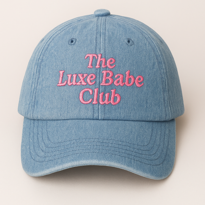 Blue denim cap with 'The Luxe Babe Club' text in pink on a beige background